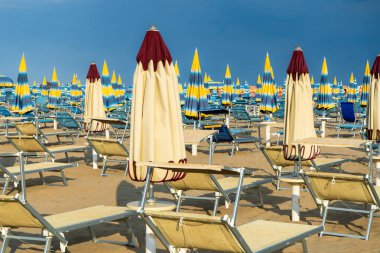 Kumsaldaki güneş pansiyonları. Boş sahil beldesi. İtalya Rimini. Sahil şeridi şezlongları güneşlenme şemsiyeleri. Yazın mavi yağmurlu gökyüzü