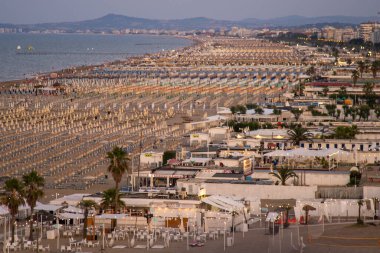 Geniş kumlu sahil, sıralı güneş panelleri ve şemsiyeler yukarıdan görünüyor. Rimini İtalyan sahilinde akşam. İtalya, Rimini - 16 Temmuz 2025