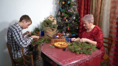 Büyükannem ve torunum birlikte Noel çelengi yapıyorlar. Yaşlı kadın ve genç çocuk konuşuyor. Aile evde. Kış gemisi