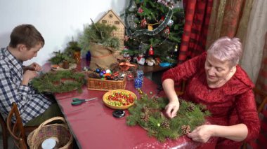 Büyükannem ve torunum birlikte Noel çelengi yapıyorlar. Yaşlı kadın ve genç çocuk kendi elleriyle dekore ederler. Aile işi araç. Noel ağacı topları