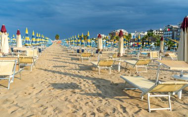 Şemsiyelerle kumlu sahilde güneşleniyorlar. Boş sahil beldesi. İtalya. Sahil şeridi şezlongunda güneş banyosu. Mavi gökyüzü yazı