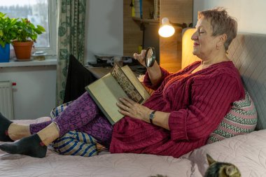 Evde Büyüteçle Kitap Okuma ve Posta Damgaları İzleme Hobisi. Yatakta oturuyor. Büyükanne keyfine bak.