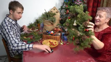 Büyükannem ve torunum birlikte Noel çelengi yapıyorlar. Yaşlı bir kadın ve genç bir çocuk birlikte vakit geçiriyorlar. Kışlık uçak evde. Firavun dalları