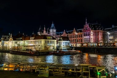 Amsterdam Tren İstasyonu geceleri Hollanda 'da kanal suyu teknesi inşa eder. Gece sokak mimarisi. Pencere fenerlerinde ışıklar..