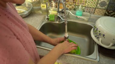 Mutfak lavabosunda elma yıkayan yaşlı bir kadın. Evde yemek pişirmek.