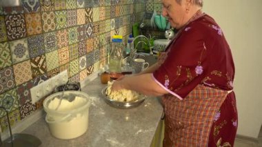 Yaşlı bir kadın, elleri masada kasede hamur yoğuruyor. Evde yemek pişirmek..