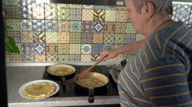 İnce krepleri kızartma tavasında kızartan bir kadın. Gel-git krep günü. Büyükannem mutfakta yemek pişiriyor. Evde fırın