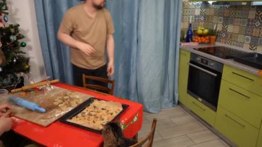 Adam fırını açar ve bir tepsi kurabiye çıkarır. Bir aile birlikte bir Noel yemeği hazırlar. Evde yemek pişir.