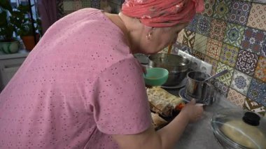 Evde yemek pişiren yaşlı bir kadın. Turtaların tepesini yumurtalarla fırçala.