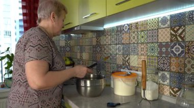 Kasenin üzerinde bıçakla yumurta kırmak. Yaşlı kadın hamur yoğuruyor. Un masanın üstünde. Evde yemek pişirmek..