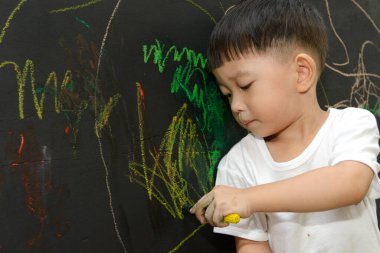Küçük şirin Asyalı çocuk elleriyle tahtaya resim çizmekten zevk alıyor.