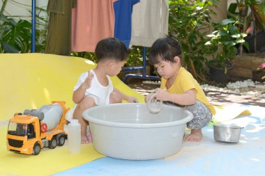 Asyalı çocuk ve kız bahçede oyuncak ve kum oynuyorlar.