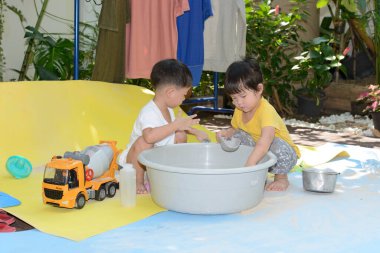 Asyalı çocuk ve kız bahçede oyuncak ve kum oynuyorlar.