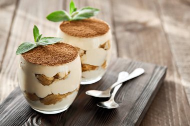 Tiramisu tatlısı, güneşli bir günde tahta bir tahtanın üzerinde bardakta..