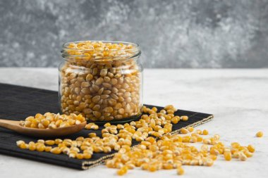 Siyah kesme tahtasının üzerinde kaşık olan cam mısır taneleri kavanozu.