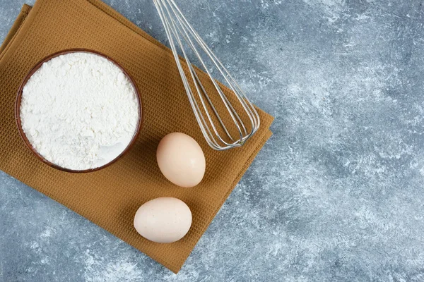 A wooden bowl of flour with two fresh chicken eggs and whisk — Stock Photo, Image