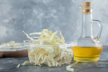 Gri arka planda doğranmış yeşil lahana ve bir şişe yağ.