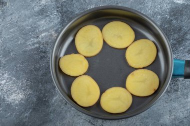 Gri arka planda, siyah tavanın içinde dilimlenmiş patates.