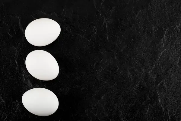 Tres huevos blancos sobre fondo negro — Foto de Stock