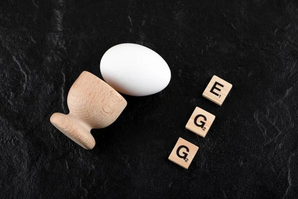 Huevo simple y carta de madera deletreada como huevo sobre fondo negro — Foto de Stock