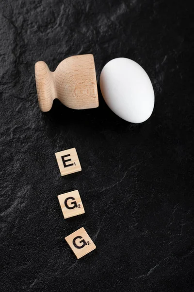 Huevo simple y carta de madera deletreada como huevo sobre fondo negro — Foto de Stock