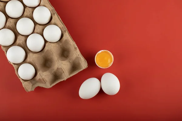 Kartong med vita ägg med äggula på röd bakgrund — Stockfoto