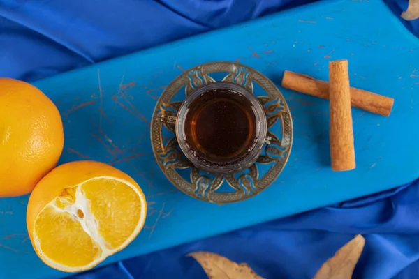 Vaso de té, naranja y palitos de canela sobre tabla azul — Foto de Stock
