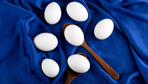 Stelletje rauwe eieren met houten lepel op blauwe satijnen doek — Stockfoto