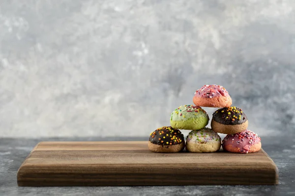 Rosquillas dulces coloridas con salpicaduras en una tabla de cortar de madera —  Fotos de Stock