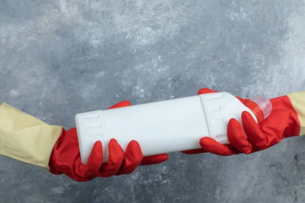 Mani in guanti rossi tenendo detersivo su sfondo di marmo — Foto Stock