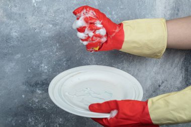 Eller kırmızı koruyucu eldivenlerle, tabağı süngerle yıkıyor.