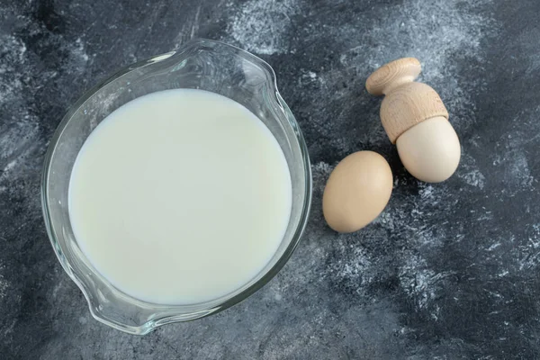 Cuenco de vidrio lleno de leche fresca y huevos sobre fondo de mármol —  Fotos de Stock