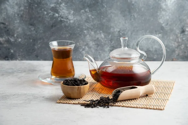 Stock image A glass cup of tea with dried loose teas and teapot