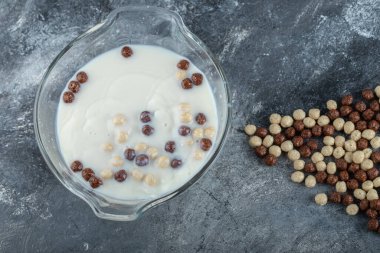 Mermer zemin üzerinde çikolata topları olan bir kase taze süt.