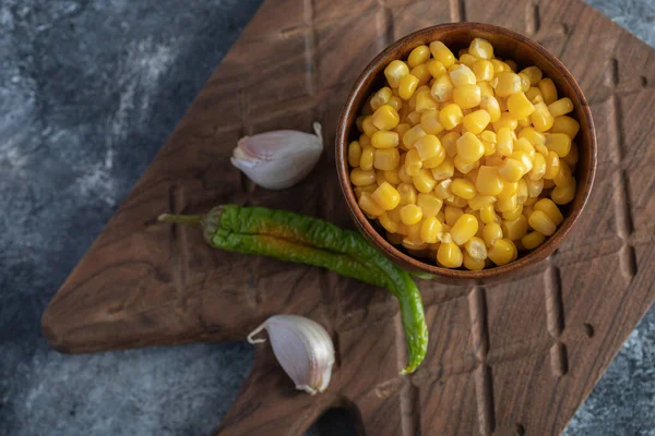 Bowl of canned corn, garlic and pepper on wooden board — Stock Photo, Image