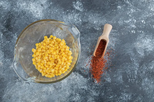 Glass bowl of canned corns and spoon of ground pepper — Stock Photo, Image