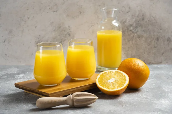 Glass cups of orange juice and a wooden reamer — Stock Photo, Image