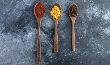 Tahta kaşık mısır taneleri, toprak ve mermer yüzeyde tahıl biberleri.