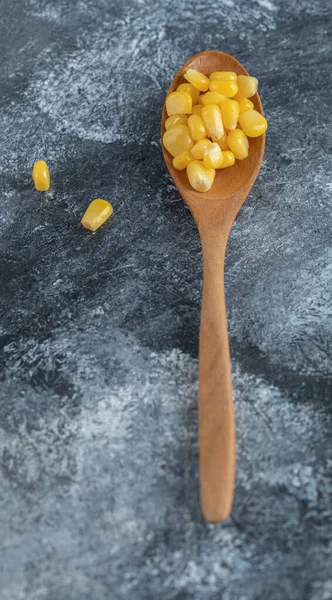 A wooden spoon full of popcorn seeds on a marble background — Stock Photo, Image