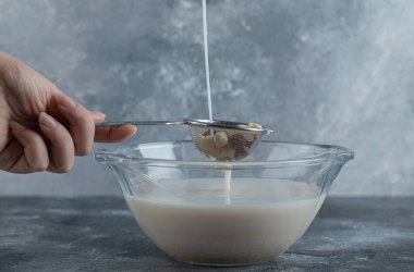 Kadın eli mısır gevreği dolu kaşığa süt ekliyor.