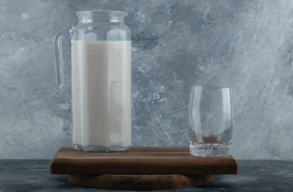 Jarro de leite fresco e copo de água em tábua de madeira — Fotografia de Stock
