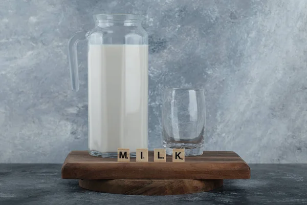 Egy kancsó tej és egy pohár víz fából készült táblán. — Stock Fotó