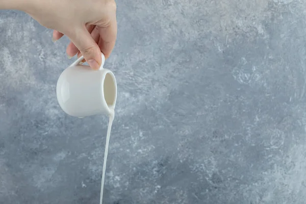 Weibliche Hand gießt frische Milch aus kleinem Becher — Stockfoto