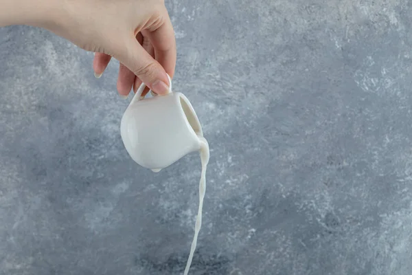 Weibliche Hand gießt frische Milch aus kleinem Becher — Stockfoto