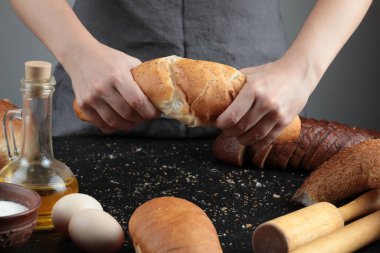 Ekmeği ikiye bölen kadın yumurta, un kasesi ve bir bardak yağ ile karanlık bir masada.