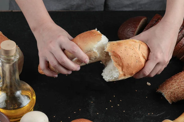 Жінка нарізала хліб навпіл на темний стіл з яйцями і склянкою олії — стокове фото
