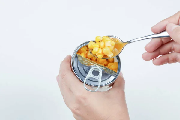 Hand taking a spoon of boiled sweet corn from a tin can on a white background — Stock Photo, Image