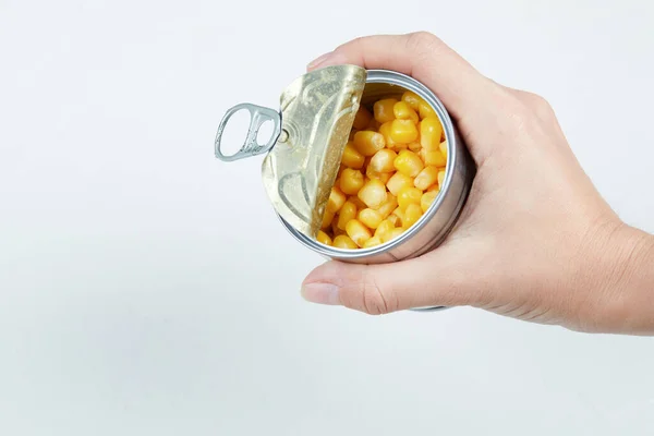Mão segurando uma lata de milho doce fervido em um fundo branco — Fotografia de Stock