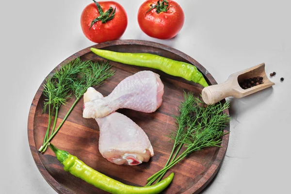 Pernas de frango cruas em chapa de madeira com verduras, tomate, alho, pimentas e limão — Fotografia de Stock