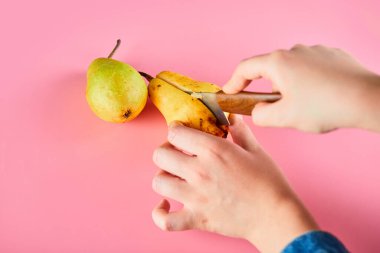 Pembe arka planda bıçakla olgun armudu doğramak.
